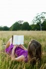 Giovane donna che legge un libro in un campo — Foto stock