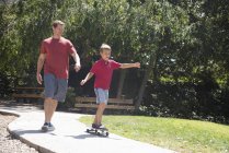Junge übt mit Vater auf Skateboard im Park — Stockfoto