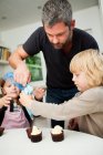 Mitte erwachsener Mann und Familie dekorieren Cupcakes mit Sahnehäubchen — Stockfoto
