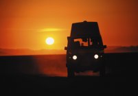 Camper van with lights silhouette at sunset sky — Stock Photo