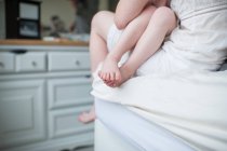 Дочка сидить на материнському коліні, обрізаний склад голих ніг і ніг — стокове фото
