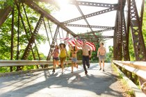 Группа друзей, бегущих по мосту с американским флагом — стоковое фото