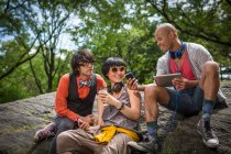 Trois amis assis sur des rochers avec lecteur mp3 et tablette — Photo de stock