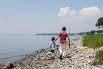 Father and son walking along beach with fishing rods — Stock Photo