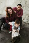 Familie mit Baby sitzt auf Treibholz am Strand — Stockfoto