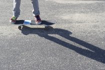 Деталь ног на скейтборде на асфальте с тенью — стоковое фото