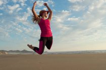 Молода жінка стрибає в повітрі на пляжі — стокове фото