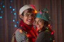 Young couple wrapped in decorative lights at christmas — Stock Photo