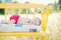 Newborn baby girl lying on yellow bench in field — Stock Photo