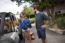 Young couple and dog preparing to load jeep for road trip — Stock Photo