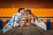 Romantic couple having a good time kissing by picnic table in amusement park — Stock Photo