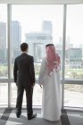 Empresarios occidentales y del Medio Oriente por ventana de la oficina de dubai - foto de stock