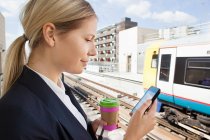 Businesswoman with coffee and smart phone in train station — Stock Photo