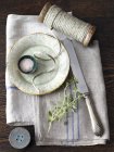 Saucer, string, knife and herbs on kitchen towel — Stock Photo