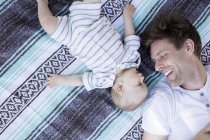 Pai e filho deitados em cobertor, face a face, vista aérea — Fotografia de Stock