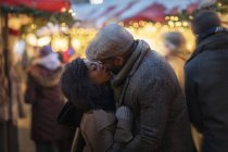 Romantic happy couple enjoying city during winter holidays kissing in outdoor market — Stock Photo