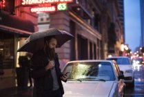 Mann zu Fuß in der Stadt in der Nacht, mit Regenschirm, Blick auf Smartphone, Innenstadt, San Francisco, Kalifornien, USA — Stockfoto