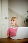 Boy looking up from laptop on desk — Stock Photo