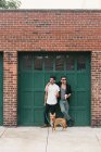 Young male couple with dog leaning on garage, eating ice cream cones — Stock Photo