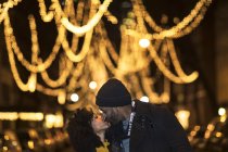Romantic happy couple enjoying city during winter holidays kissing under outdoor holiday lights — Stock Photo