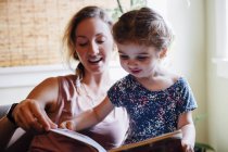 Frau auf Sofa mit Kleinkind-Tochter beim Bilderbuchlesen — Stockfoto