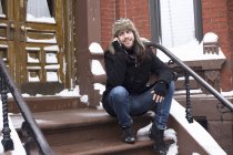 Junger Mann plaudert auf Smartphone vor verschneiter Haustür — Stockfoto