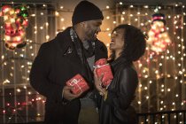 Романтическая счастливая пара наслаждаясь городом во время зимних праздников проведение подарков перед праздничными огнями — стоковое фото