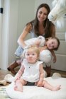 Portrait of baby girl sitting on floor with mother and sister behind — Stock Photo
