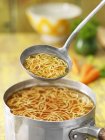 Close up of saucepan and ladle with noodle soup — Stock Photo