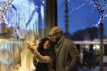 Romántico feliz pareja disfrutando de la ciudad durante las vacaciones de invierno ventana de compras - foto de stock