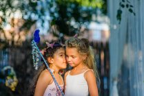 Dos chicas jóvenes vestidas de hadas, niña susurrando al oído de un amigo - foto de stock