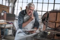 Cape Town, South Africa, elderly craftsman in workshopon a call — Stock Photo