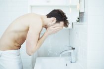 Hombre joven lavando la cara en el lavabo del baño - foto de stock