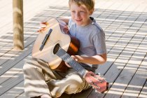 Niño tocando la guitarra en el muelle - foto de stock