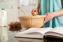 Жінка розбиває яйце миски на кухні — стокове фото
