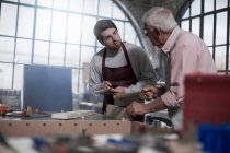 Cape Town, South Africa, young woodworker taking down notes from elderly man in workshop — Stock Photo
