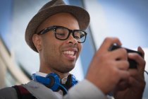 Молодой человек в шляпе и очках с помощью mp3 плеера — стоковое фото