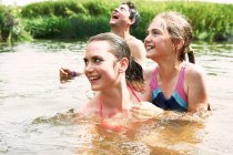 Dos hermanas y un amigo nadando en el lago rural - foto de stock