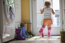 Bambino di sesso femminile che indossa stivali di gomma guardando fuori dalla finestra della porta posteriore — Foto stock
