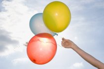 Main tenant des ballons colorés avec ciel nuageux bleu sur fond — Photo de stock
