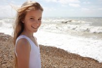 Girl on shingle beach by the sea, smiling at camera — Stock Photo