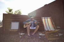 Homem adulto médio tocando guitarra em cadeira de praia na festa no telhado — Fotografia de Stock