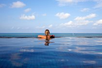 Вид ззаду жінка розслабляється в нескінченному басейні — стокове фото