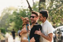 Young male couple carrying dog on suburban sidewalk — Stock Photo