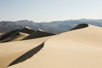 Sand dunes in sunlight with mountains on background — Stock Photo