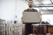 Portrait of man holding cardboard box in factory — Stock Photo