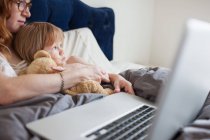 Madre e figlia sdraiate a letto con computer portatile — Foto stock