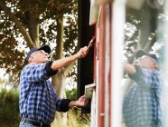 Hombre mayor pintando lado de la casa - foto de stock
