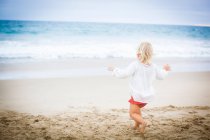 Вид сзади девочки, бегущей к морю — стоковое фото