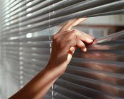 Cropped image of woman peeping through venetian blinds — Stock Photo
